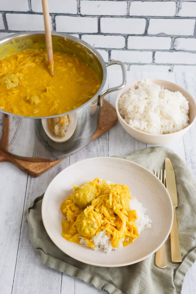 Kål i karry med kødboller og gryde i baggrunden